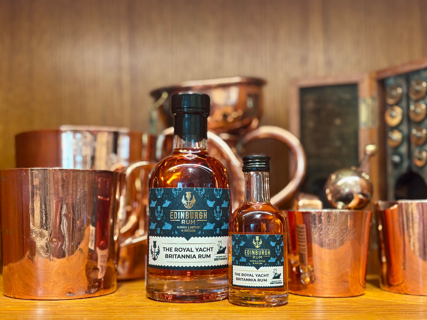 Two bottles of Edinburgh Rum on a bar counter with copper containers in the background.