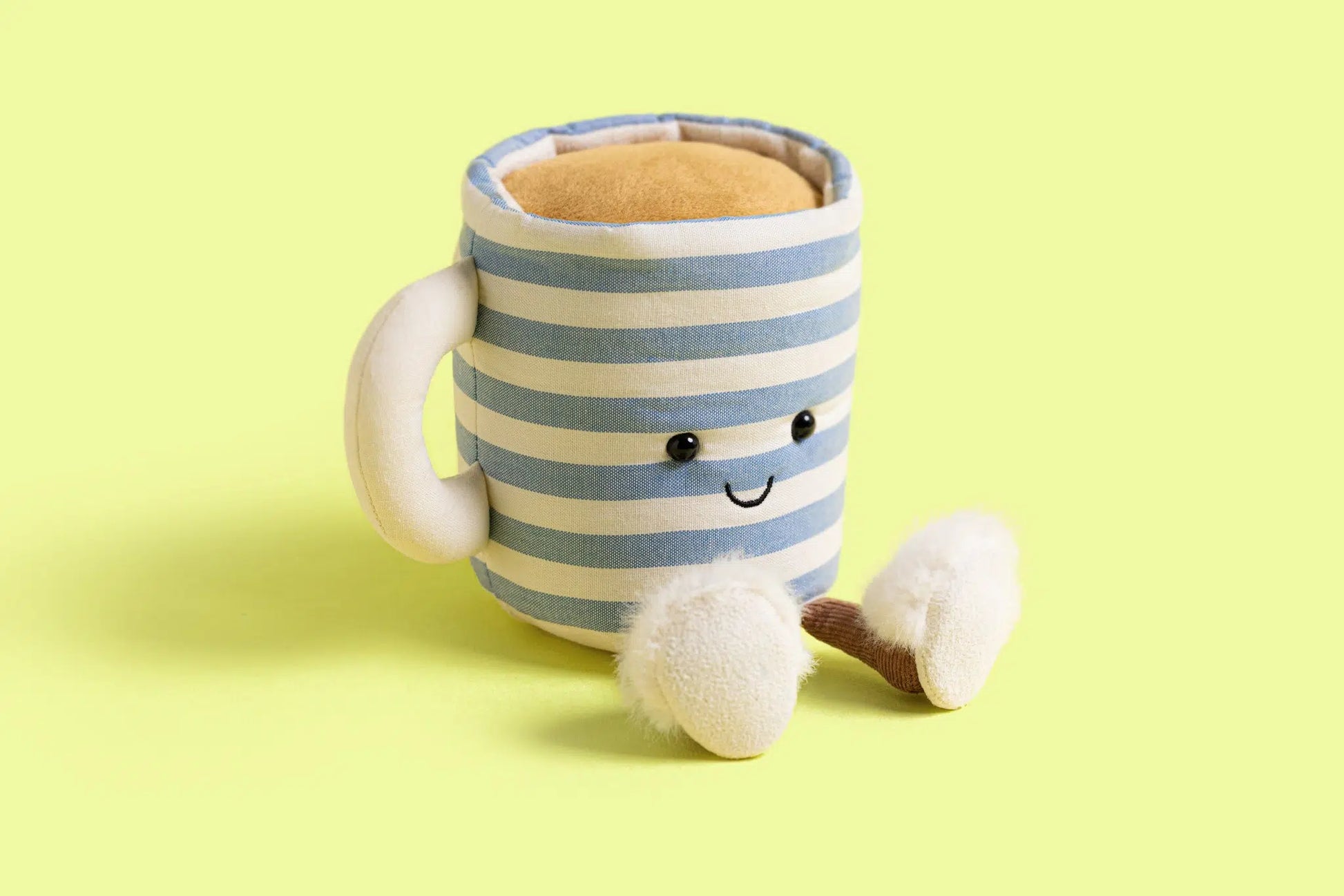 Striped mug with a smiling face and fuzzy slippers on a yellow background.